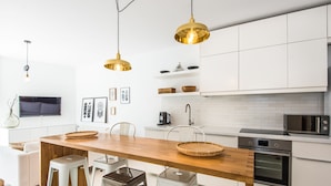 A modern kitchen with white cabinets, a wooden dining table, and two hanging pendant lights. - Super-Apartamenty Exotic (Poznan)