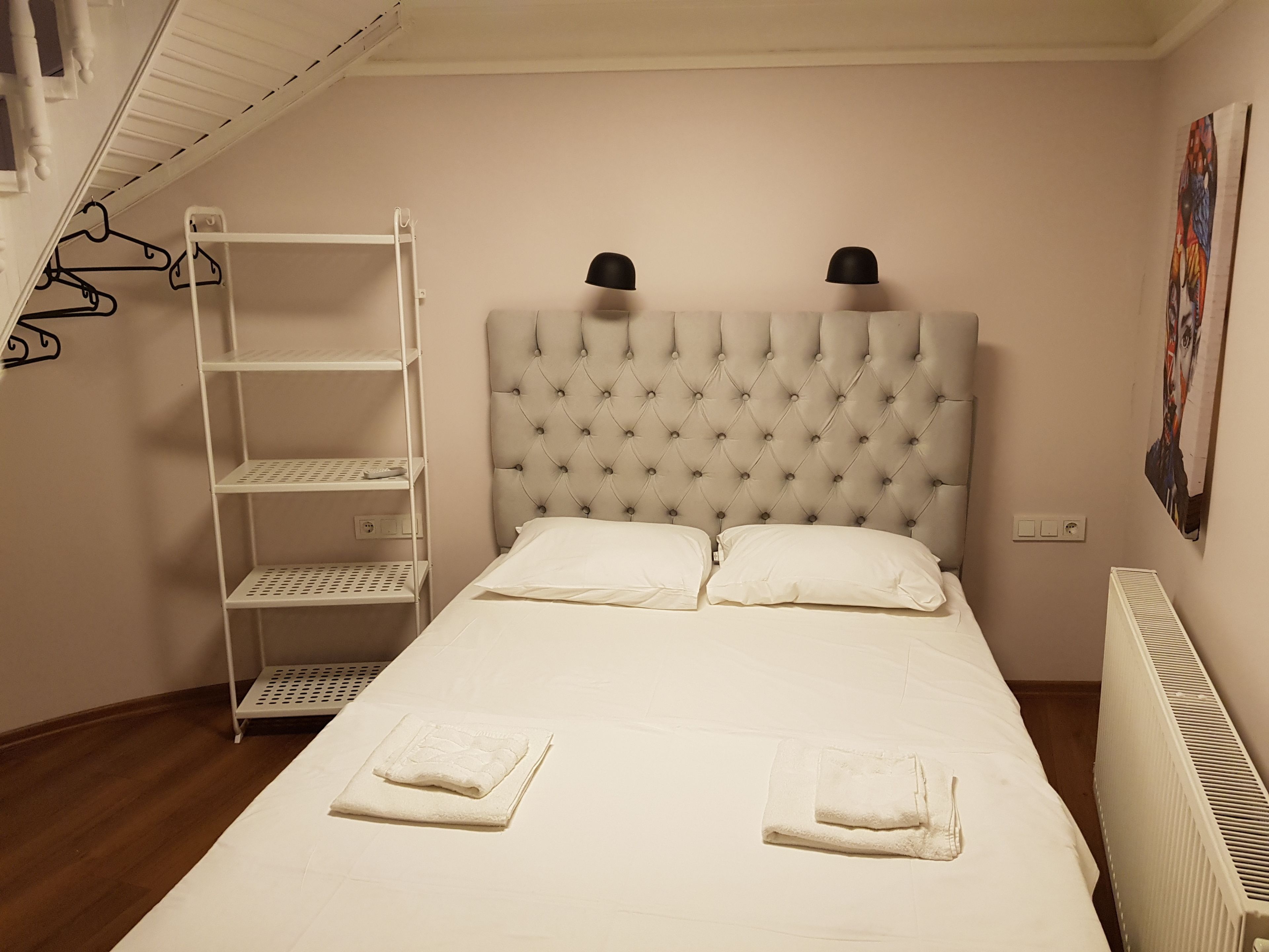 Une chambre à coucher avec une tête de lit capitonnée, un lit blanc avec deux oreillers, une étagère blanche et un radiateur.