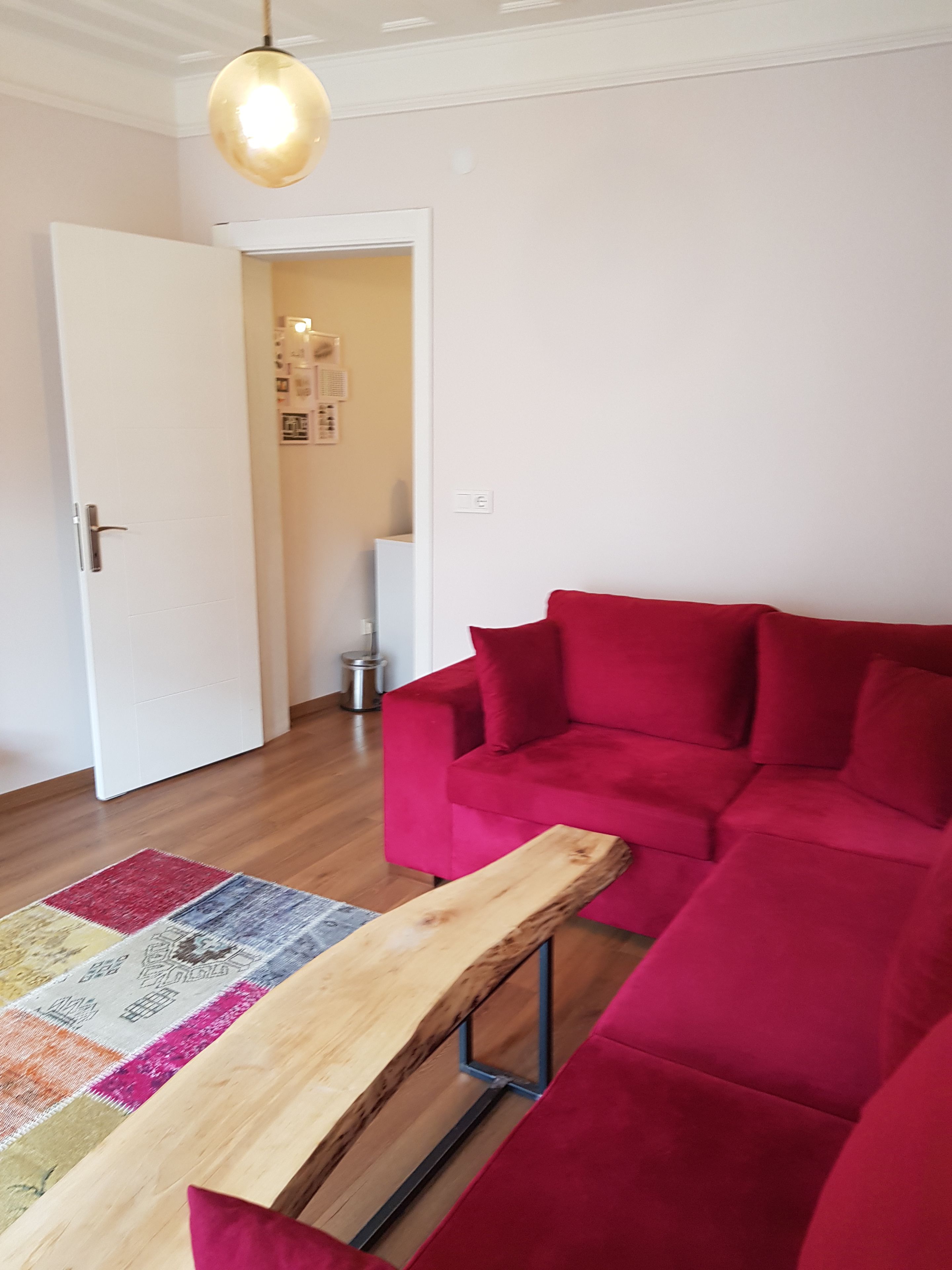 A living room with a red sofa, a wooden bench, and a patterned rug.
