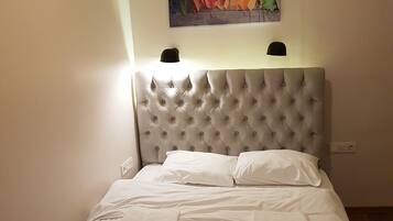 A neatly made bed with white linens and pillows, a tufted headboard, and a wall-mounted painting of colorful leaves.
