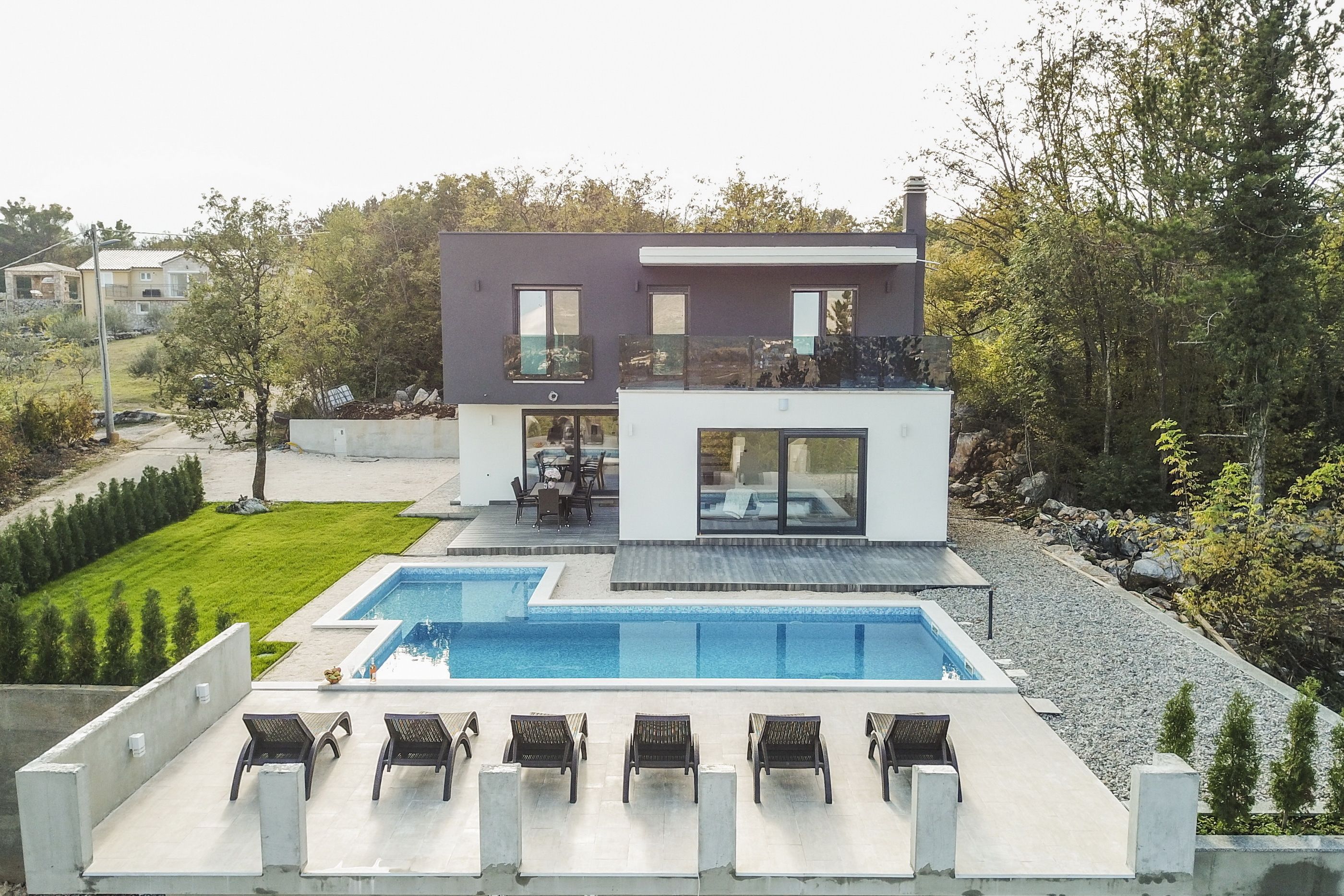 A modern two-story house with a swimming pool, outdoor seating, and a well-maintained garden.