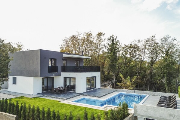 A modern two-story house with a swimming pool, a patio, and a view of trees.