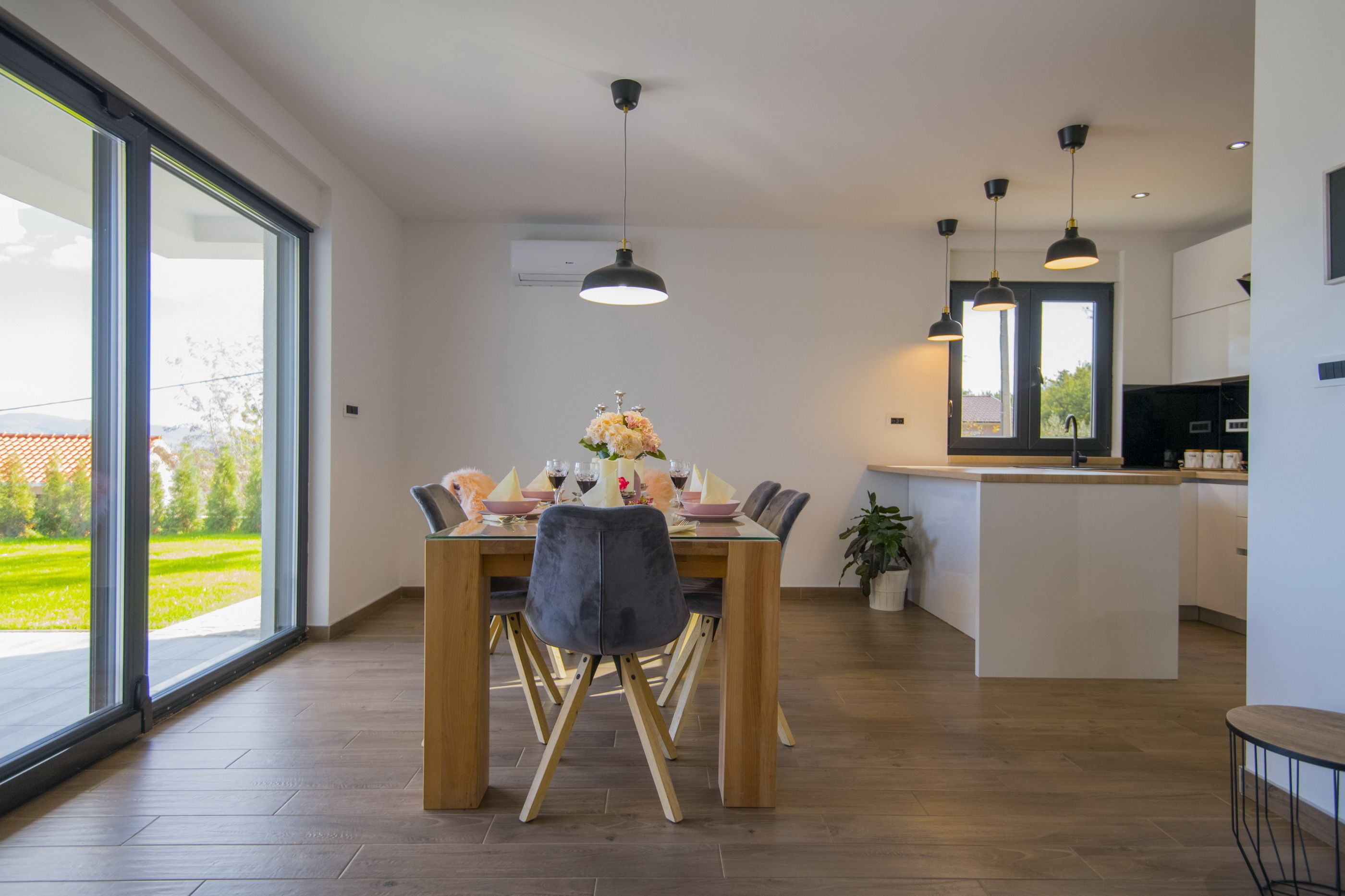 A modern dining area with a wooden table and chairs, a vase of flowers, and pendant lighting.