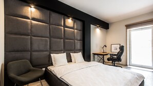 A modern bedroom with a large bed, a dark headboard, a desk, and a chair. - Super-Apartamenty Exclusive (Poznan)