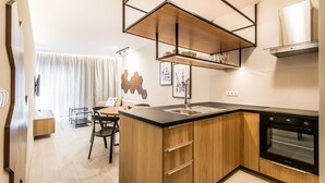 A modern kitchen with wooden cabinetry, a black countertop, a built-in oven, and a dining area with a table and chairs. - Super-Apartamenty Exclusive (Poznan)