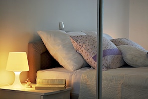 A neatly made bed with multiple pillows, a bedside lamp, and a book on a nightstand.