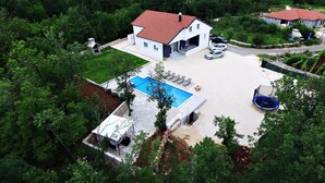 Ein zweistöckiges Haus mit Schwimmbecken, Trampolin und überdachter Terrasse.