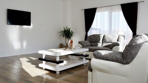 Ein modernes Wohnzimmer mit einem weißen Sofa, einem weißen Couchtisch und einem flachbildfernseher an der Wand.