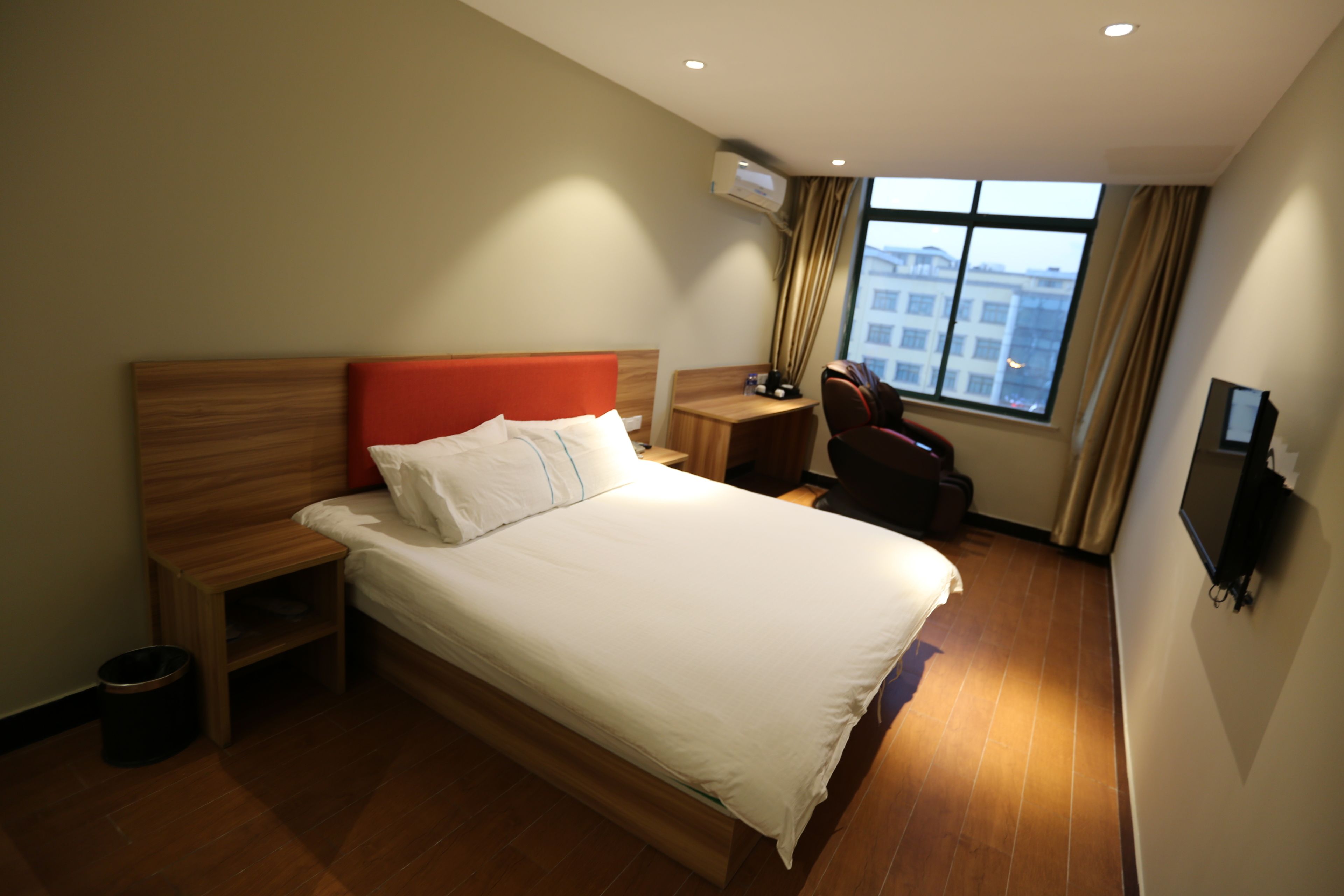 Quarto de hotel com cama grande, mesa de cabeceira de madeira, escrivaninha com cadeira, televisão e janela com cortinas.