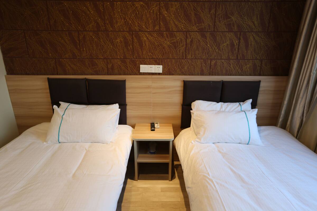 Habitación de hotel con dos camas, cabecera de madera, mesita de noche con teléfono y toma de corriente.