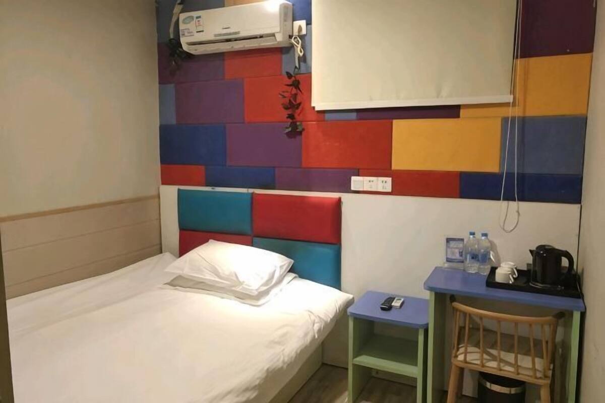 Habitación de hotel con cama, un escritorio pequeño con silla, un equipo de aire acondicionado y un diseño de pared colorido.