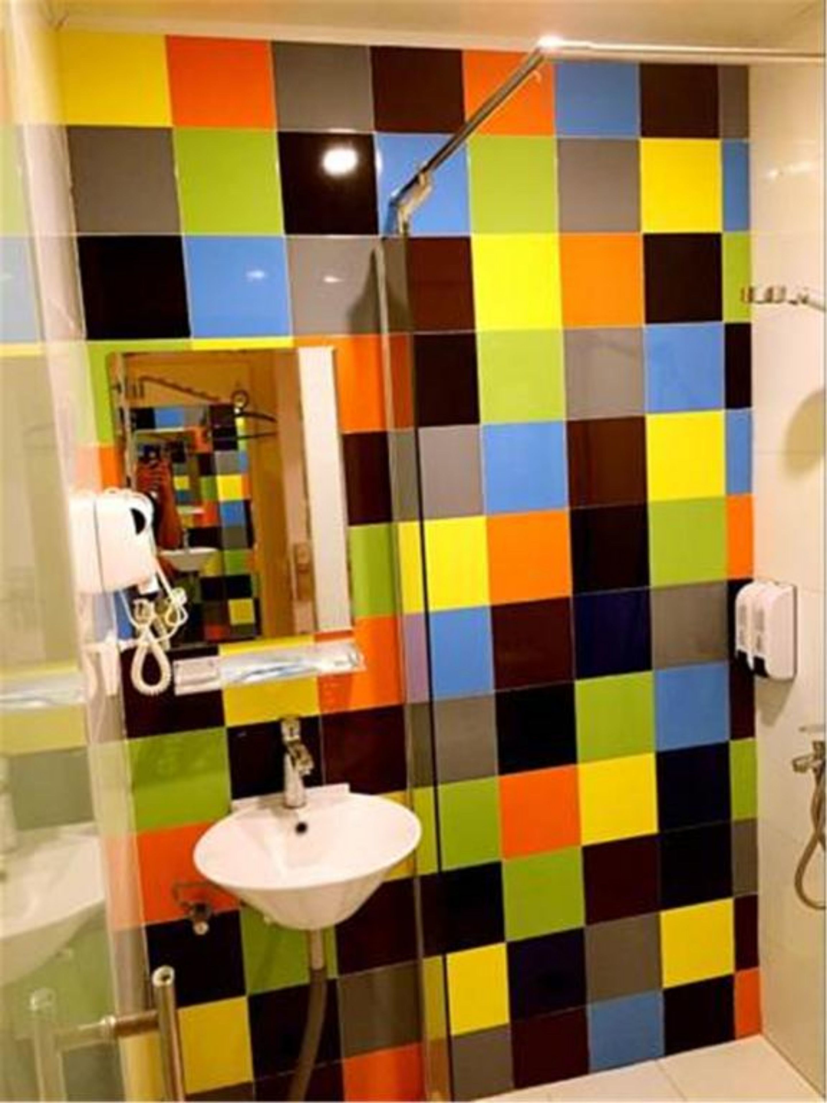 A bathroom with a colorful checkered tile wall, a glass shower enclosure, and a white sink.
