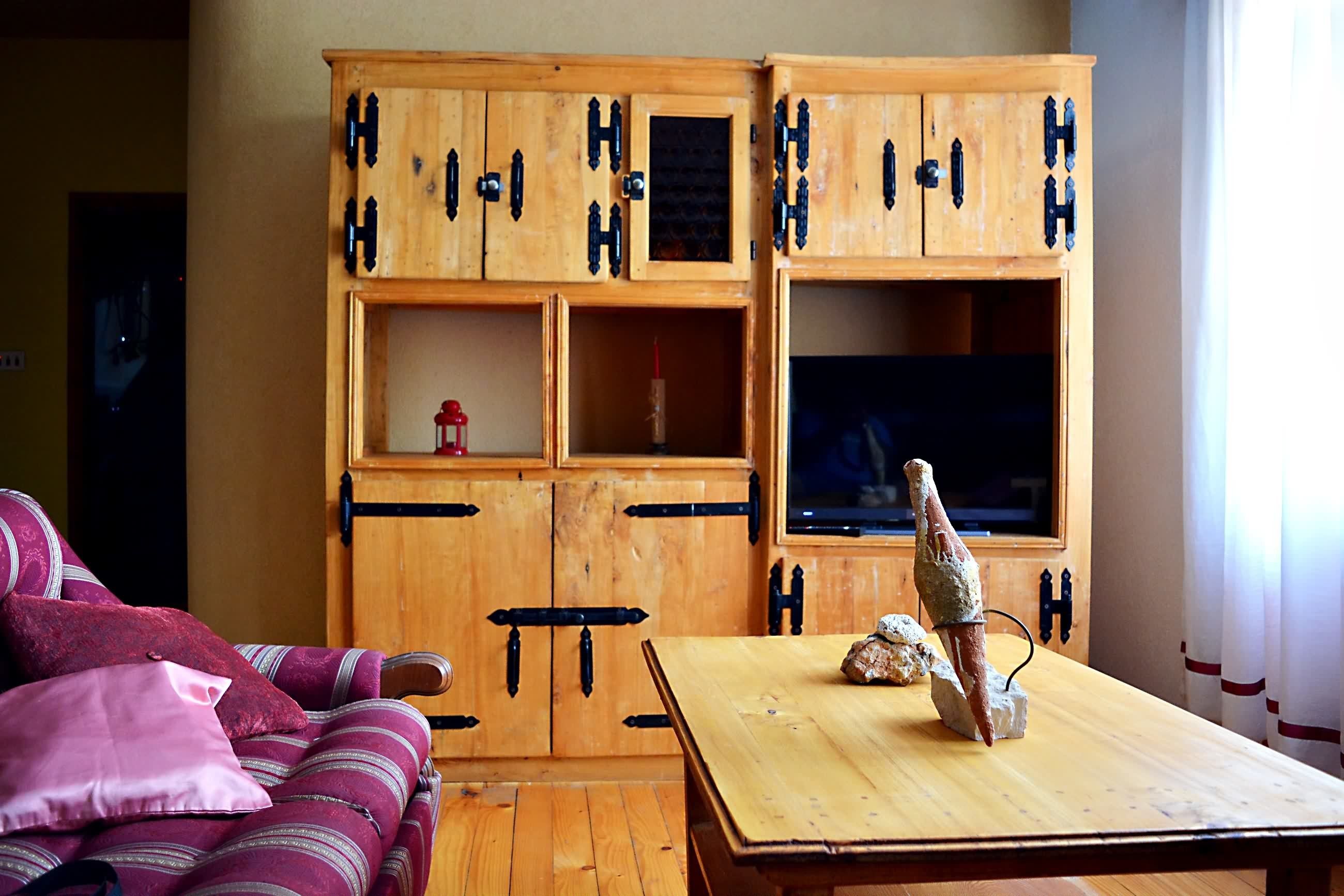 A room with a wooden cabinet, a television, a table, and a couch.
