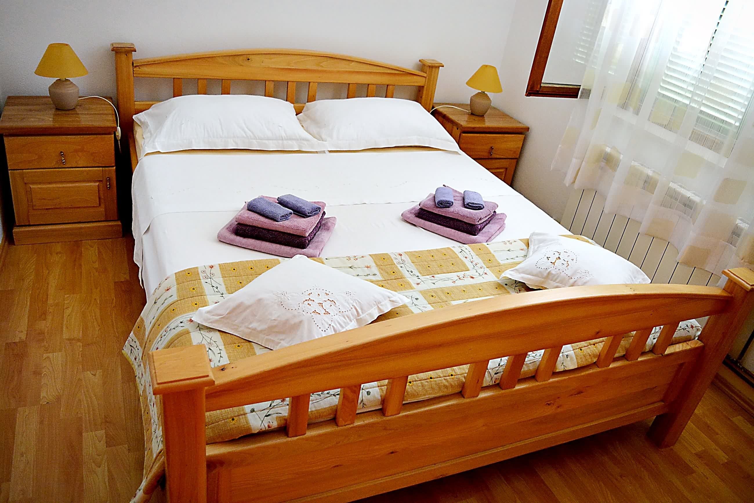 A neatly made bed with a wooden headboard, two bedside tables with lamps, and a window with blinds.