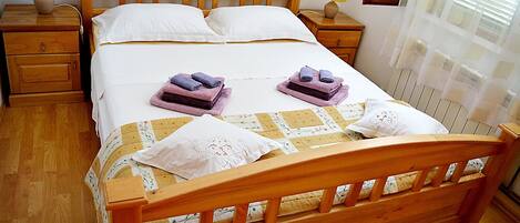 A neatly made bed with a wooden headboard, two bedside tables with lamps, and a window with blinds.