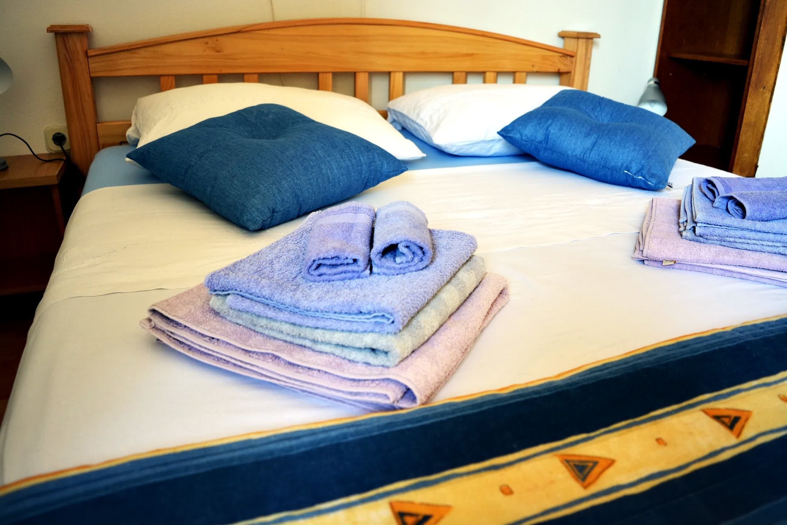 A neatly made bed with a wooden headboard, two pillows, and folded towels.
