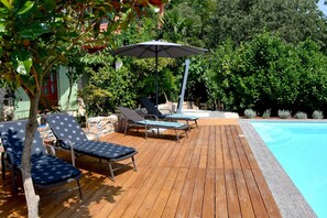 A wooden deck with lounge chairs and an umbrella, a swimming pool, and lush greenery. - Holiday House Marcel (Podbablje)