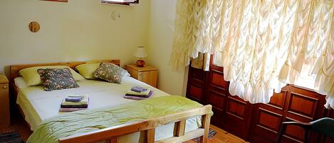 A bedroom with a wooden bed, a nightstand with a lamp, a chair, and a window with curtains.