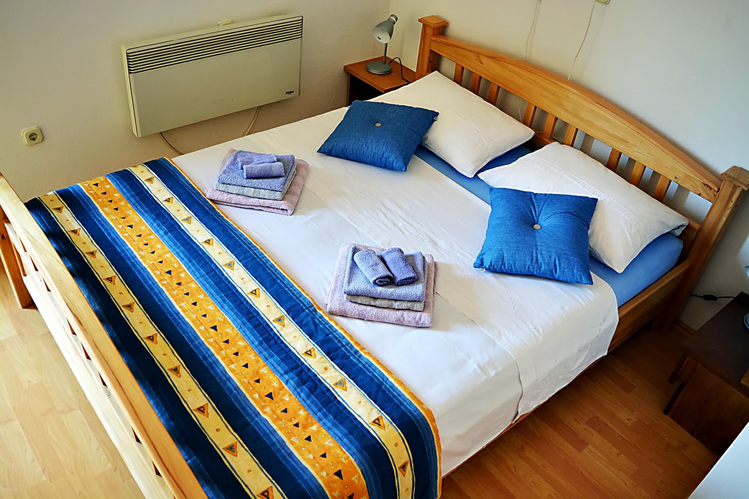 A neatly made bed with a blue and yellow striped blanket, two blue pillows, and folded towels on the bed.