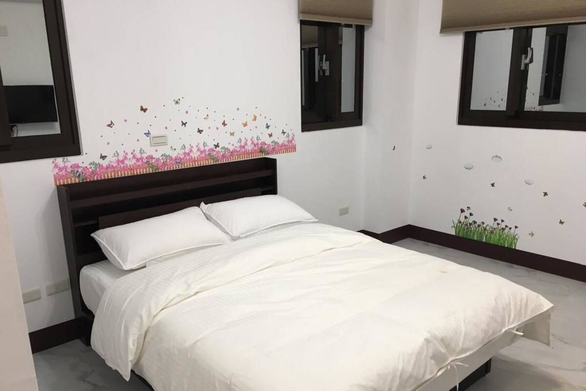 Ein Schlafzimmer mit einem Bett, weißer Bettwäsche, einem Kopfteil, einem Fenster und Wanddekorationen.