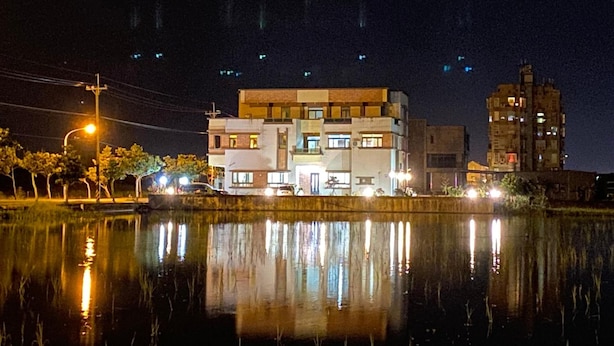 A multi-story building with a flat roof and a reflective water surface in front. - Home of 120 B&B (Jiaoxi)