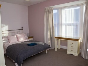 Un dormitorio con cama, escritorio y ventana con cortinas.