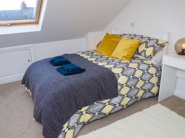 Un dormitorio con cama, almohadas, una mesita de noche y una ventana.