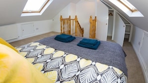 A bedroom with a sloped ceiling, skylights, a bed with a patterned bedspread, and a wooden staircase. - Jutes House Exeter (Exeter)
