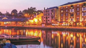 A waterfront hotel with a reflection in the calm water, featuring a dock with boats and a row of buildings with illuminated windows. - Jutes House Exeter (Exeter)