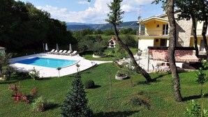 Un área de piscina con sillones de descanso, un edificio de piedra con balcón y vistas a las montañas al fondo.