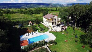 Una casa de dos pisos con piscina, rodeada de un césped cuidado y árboles.