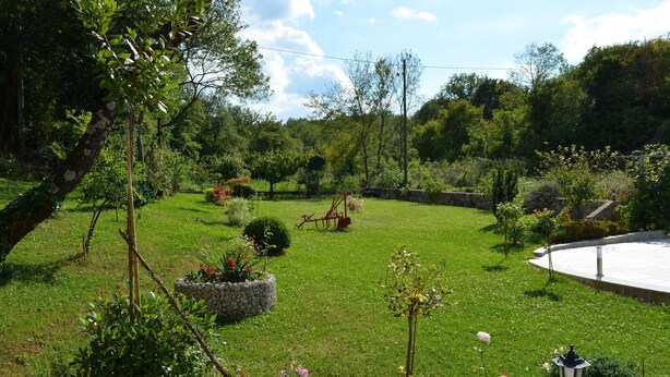 Un jardí ben cuidat amb un camí de pedra, un parc de swings i una estructura circular de pedra.