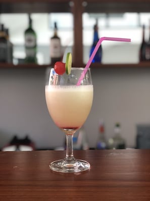 A cocktail glass with a pink straw, garnished with a cherry and a lime slice, on a wooden bar counter.