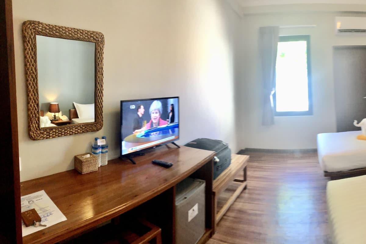 Quarto de hotel com televisão, duas camas, escrivaninha e espelho.