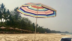 Una spiaggia con un ombrellone a righe, un cappello di paglia e un asciugamano su un tappetino giallo.