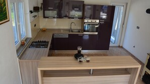 A modern kitchen with dark cabinets, a central island, and a built-in oven. - Holiday House 4M (Podbablje)