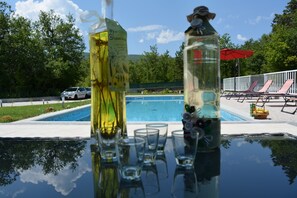 A poolside table with clear glasses and bottles, a pool, lounge chairs, and a red umbrella. - Holiday House 4M (Podbablje)