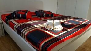 A bed with a patterned bedspread and pillows, a rolled towel, and a wooden floor. - Holiday House 4M (Podbablje)