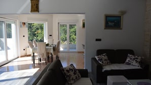 A spacious living area with a dark sofa, a small table, and a dining area with a table and chairs. - Holiday House 4M (Podbablje)
