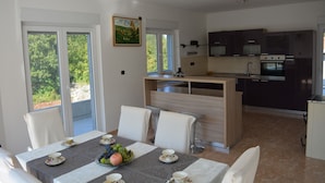 A modern kitchen with dark cabinets, a built-in oven, and a dining area with a table set for two. - Holiday House 4M (Podbablje)