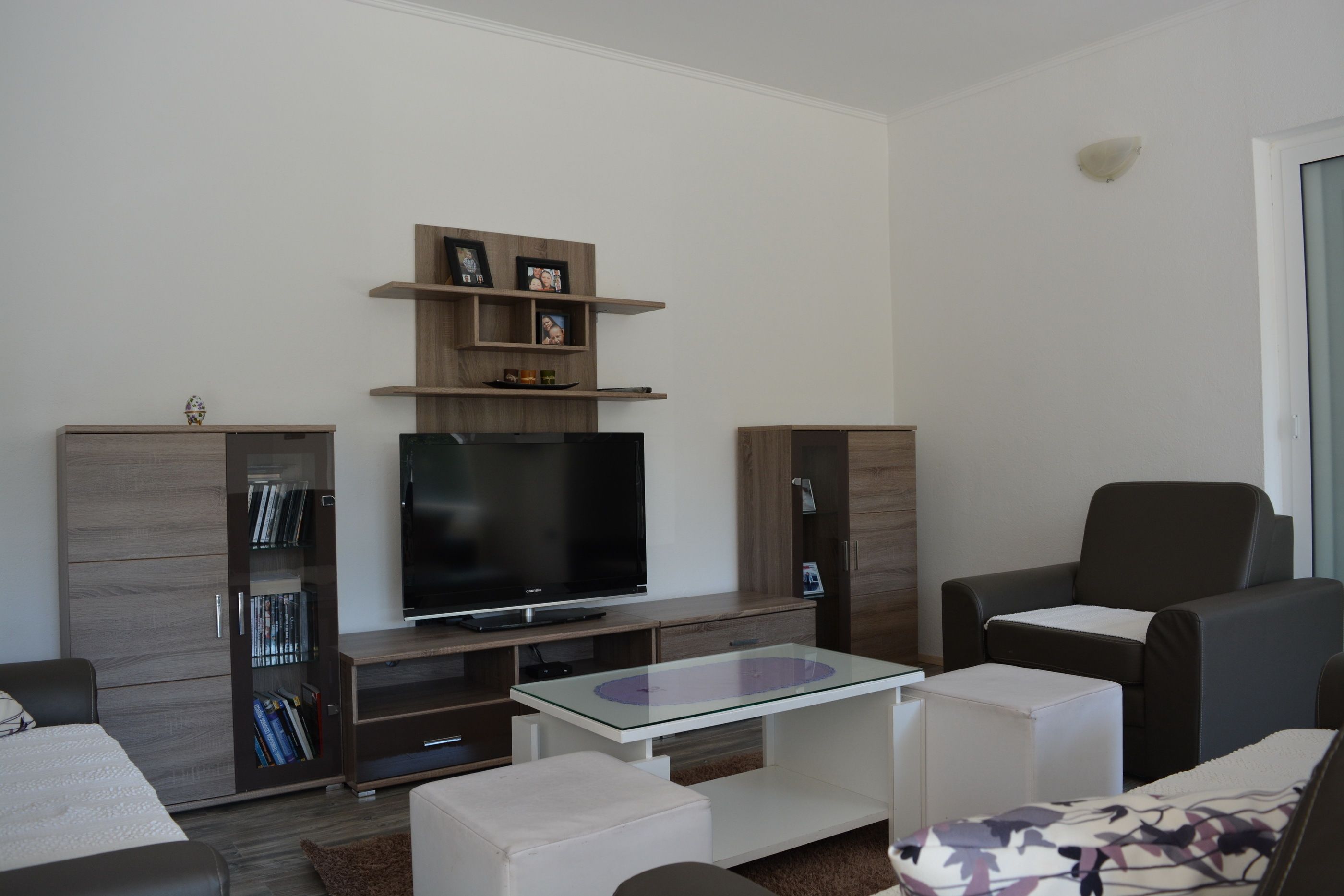 Una sala de estar moderna con un televisor de pantalla plana, una mesa de centro de vidrio y sofás de cuero oscuro.