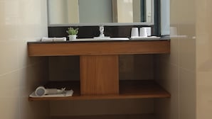 Een badkamer met een houten wastafelmeubel, een spiegel en een plank met toiletartikelen.