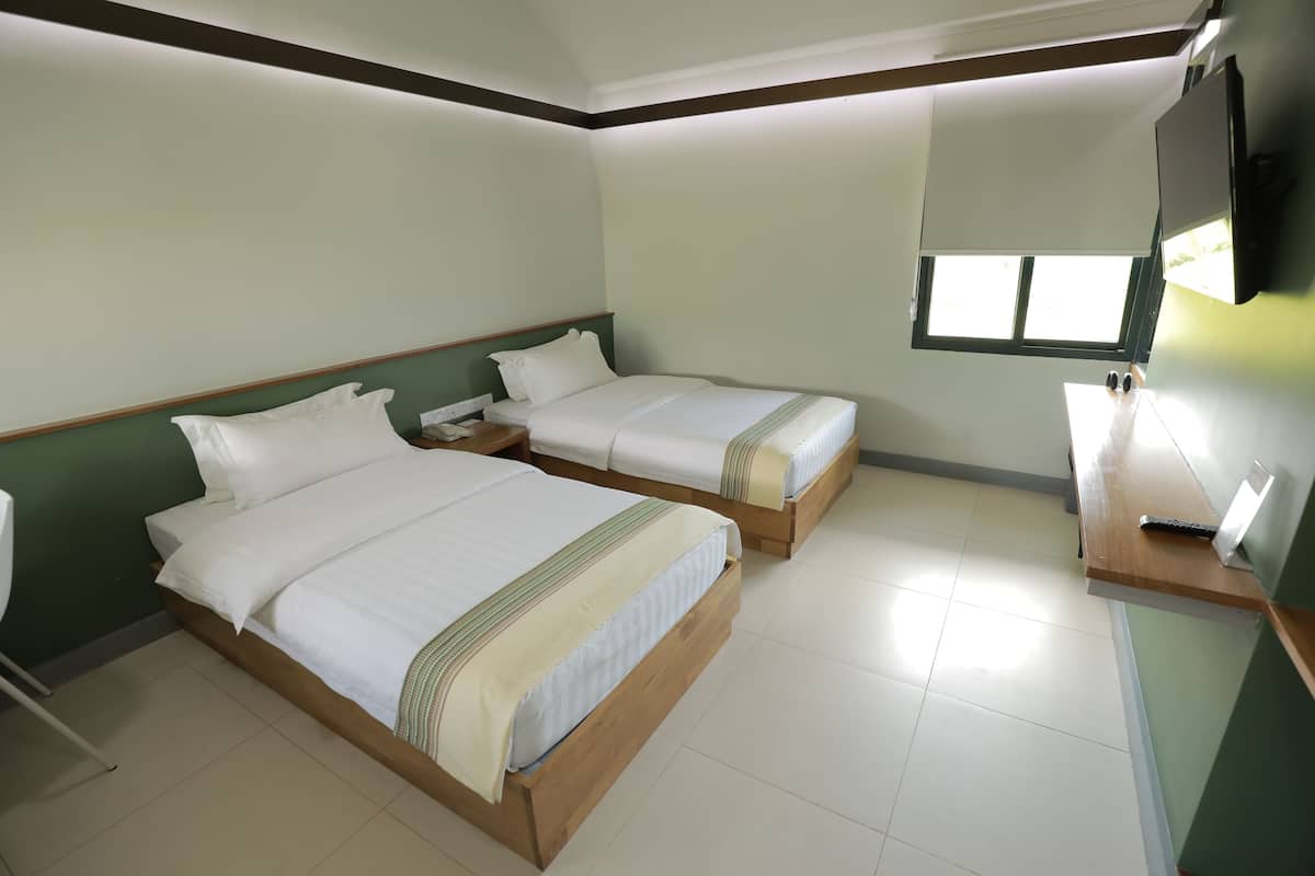 A hotel room with two wooden beds, a small desk, and a TV mounted on the wall.