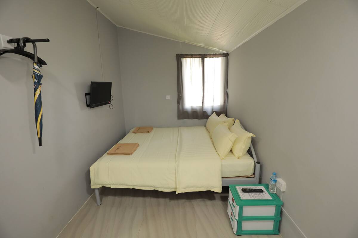 A bedroom with a bed, a window, a wall-mounted TV, and a green storage box.