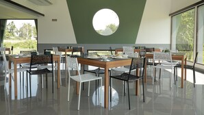 Een eetgedeelte met ronde tafels en stoelen, een groot raam en een groene accentmuur.
