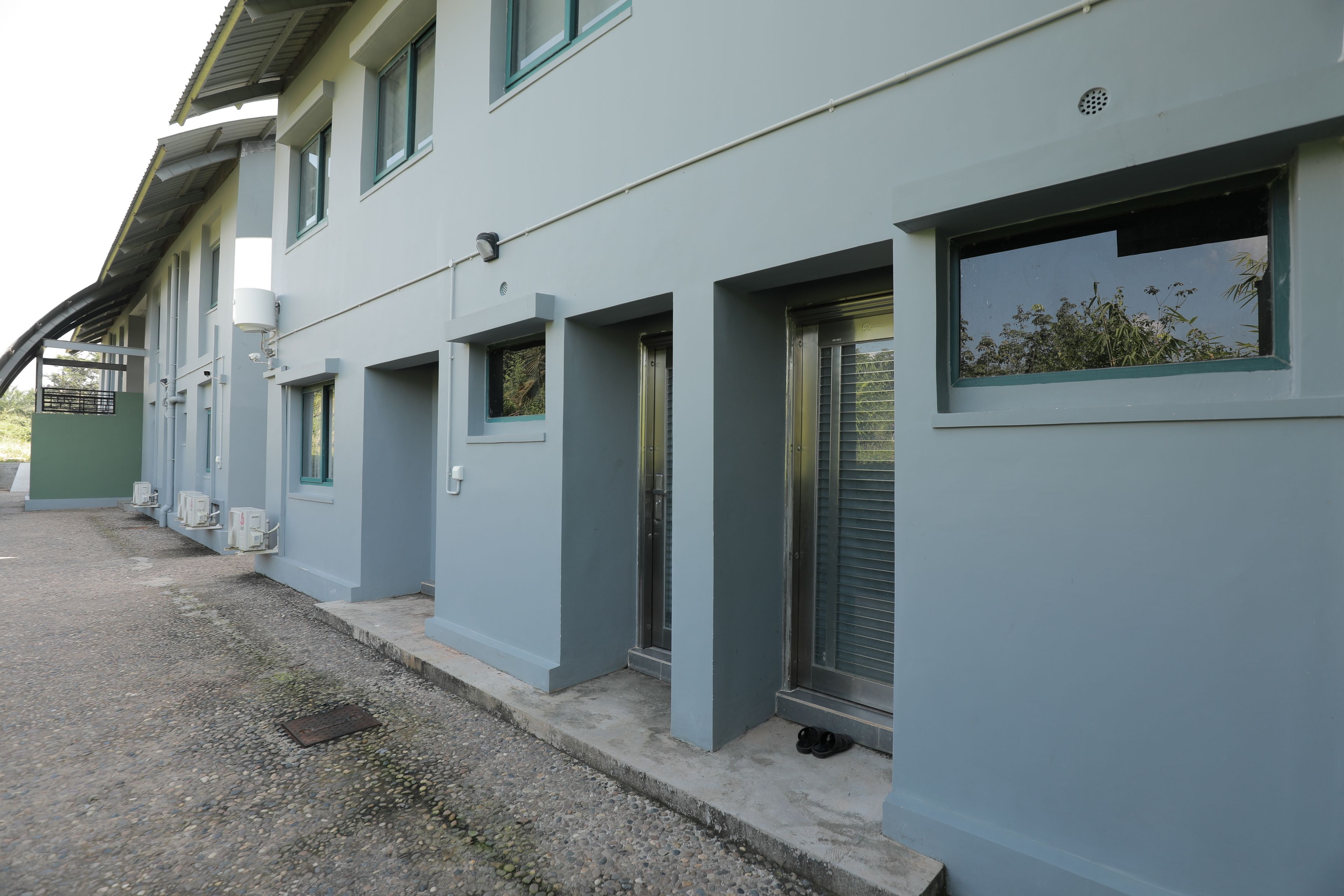 A row of light blue buildings with multiple windows and doors, some with shutters, and a gravel path in front.