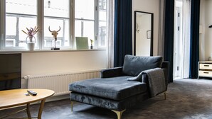 Una habitación moderna con un sofá gris, una mesita con un control remoto y una ventana con vistas al exterior.