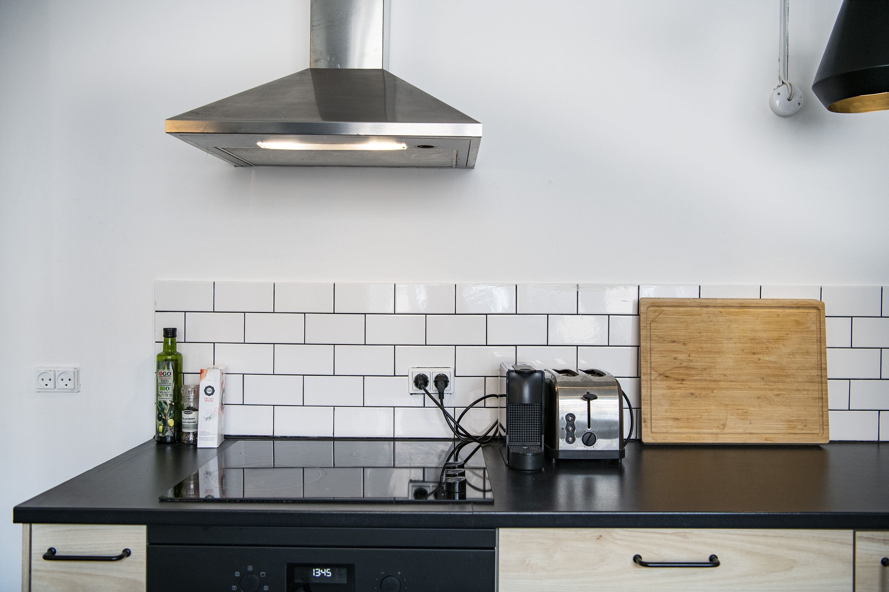 A kitchen with a black countertop, a stainless steel range hood, a toaster, a wooden cutting board, and a dishwasher.