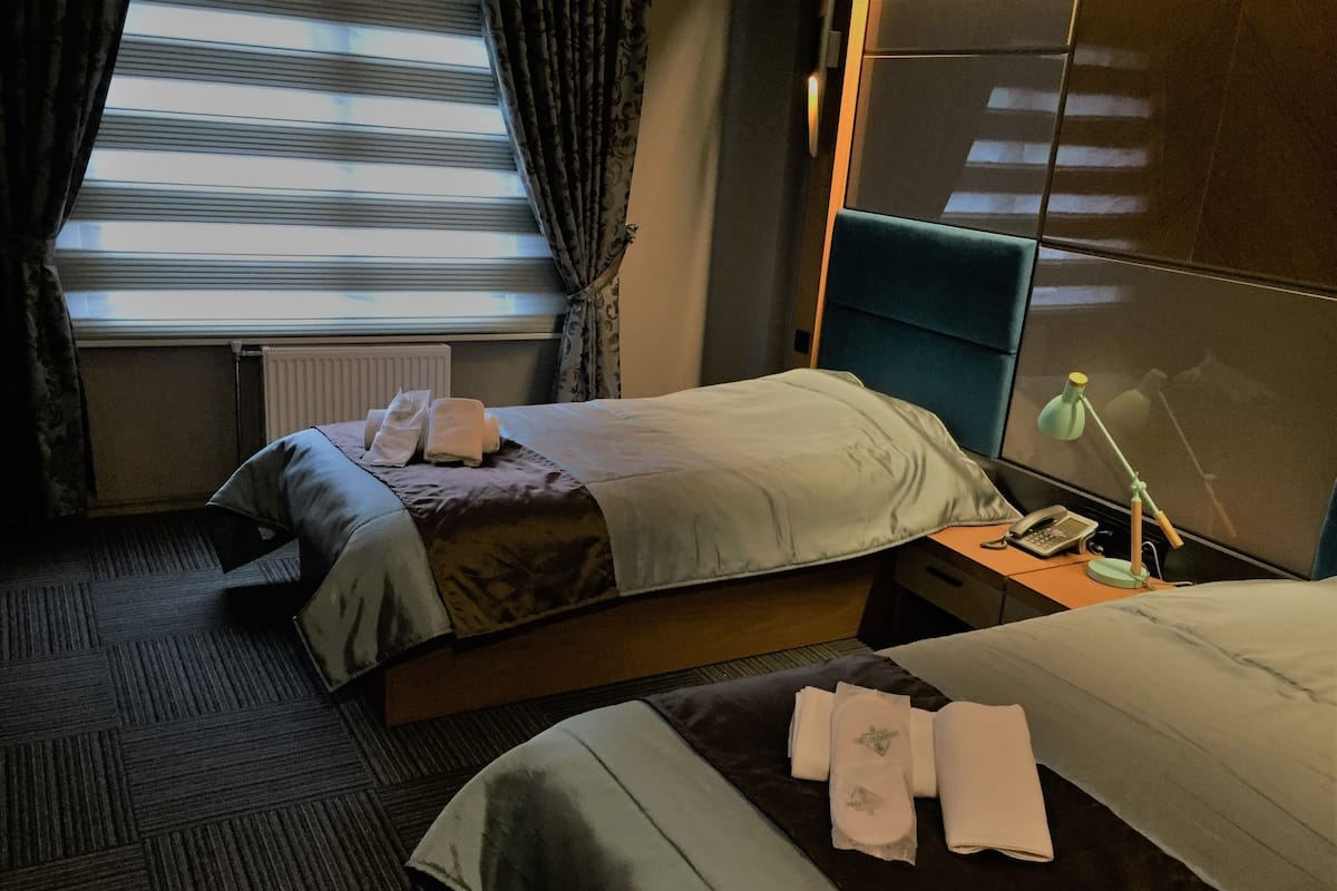 Une chambre d’hôtel avec deux lits, une table de chevet avec une lampe, un téléphone et une fenêtre avec des rideaux.