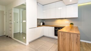 A modern kitchen with white cabinets, a wooden countertop, and a glass door leading to a shower area. - Super-Apartamenty Love Deluxe (Poznan)